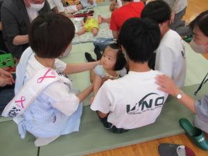 赤ちゃんに手を差し伸べる愛育委員と中学生の写真